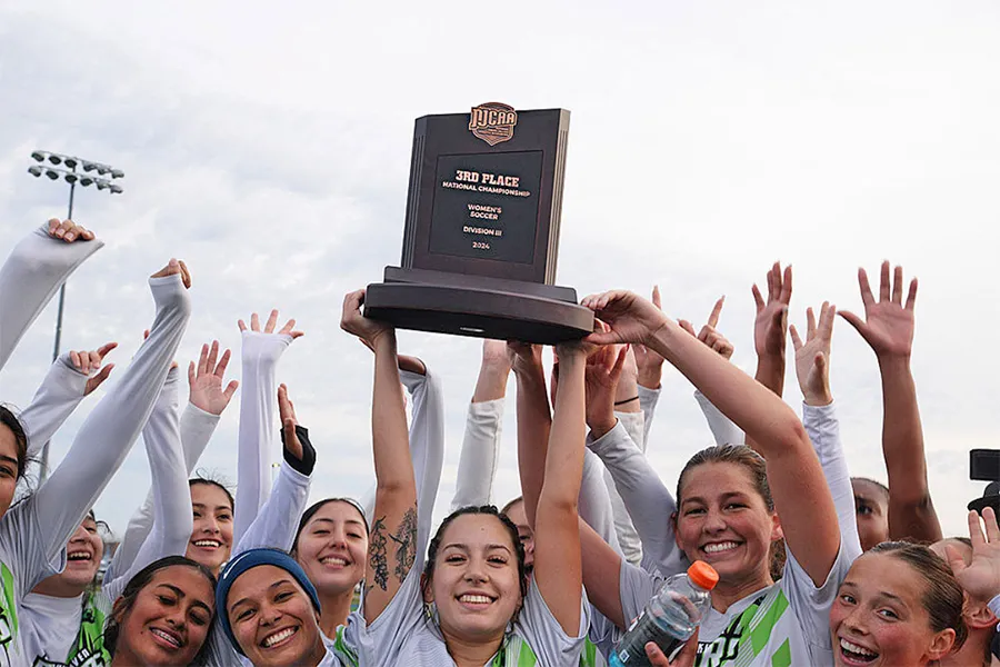 A group of Dallas College volleyball players celebrate their championship victory together on the court, posing proudly with smiles and championship energy after a successful season.
