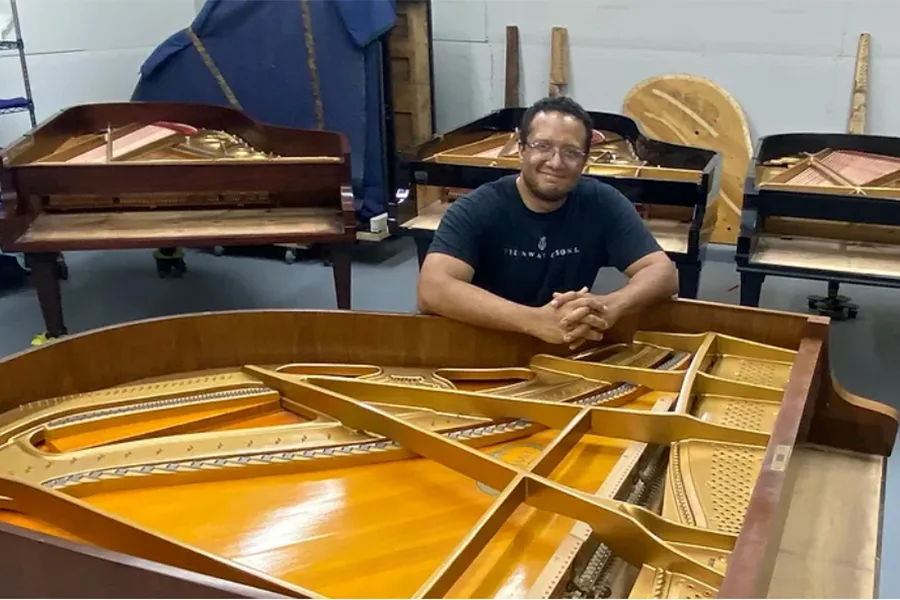 Dallas College music professor Victor Soto sits with grand pianos in his workshop, where he tries to rebuild and maintain instruments.