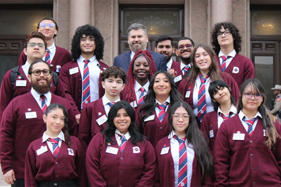 16 Dallas College Students and Chancellor Lonon stand in front of a building.