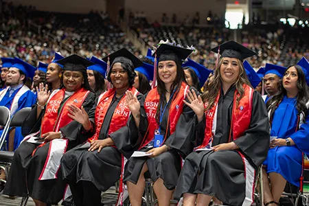 A group of nursing students sit at graduation in their caps and gowns.