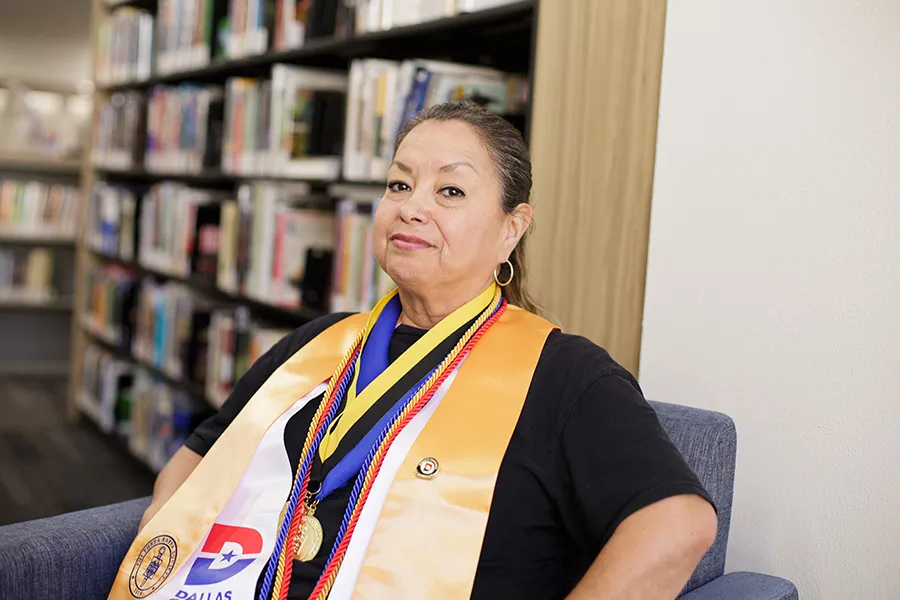 Marisol Perez sits in the library wearing her graduation regalia.