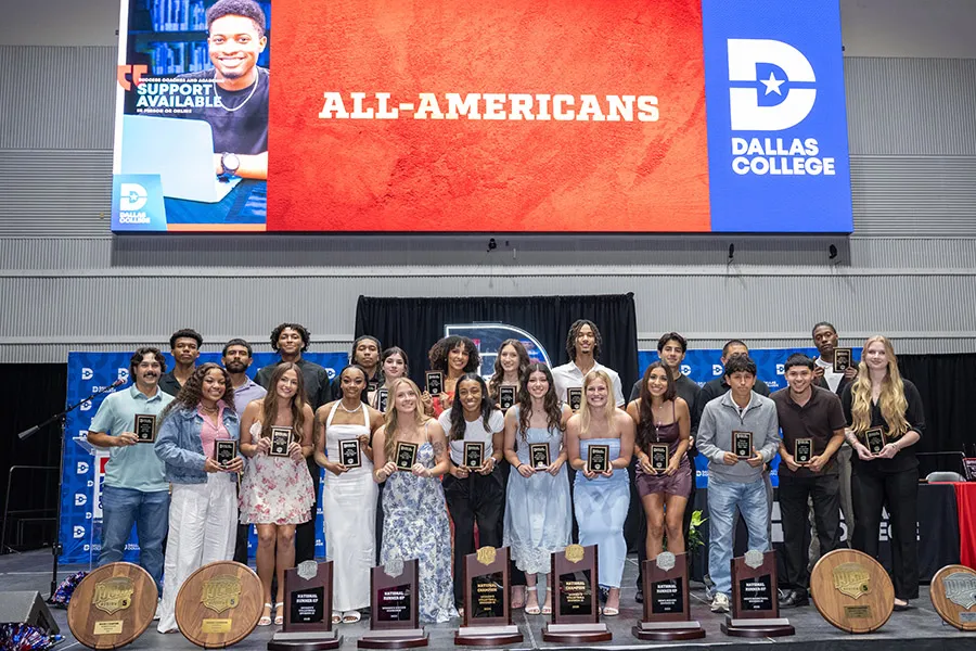 Two rows of student athletes on stage holding plaques.