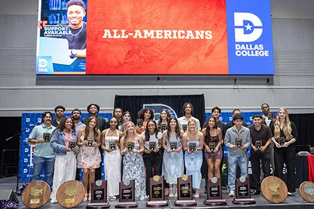 Two rows of student athletes on stage holding plaques.