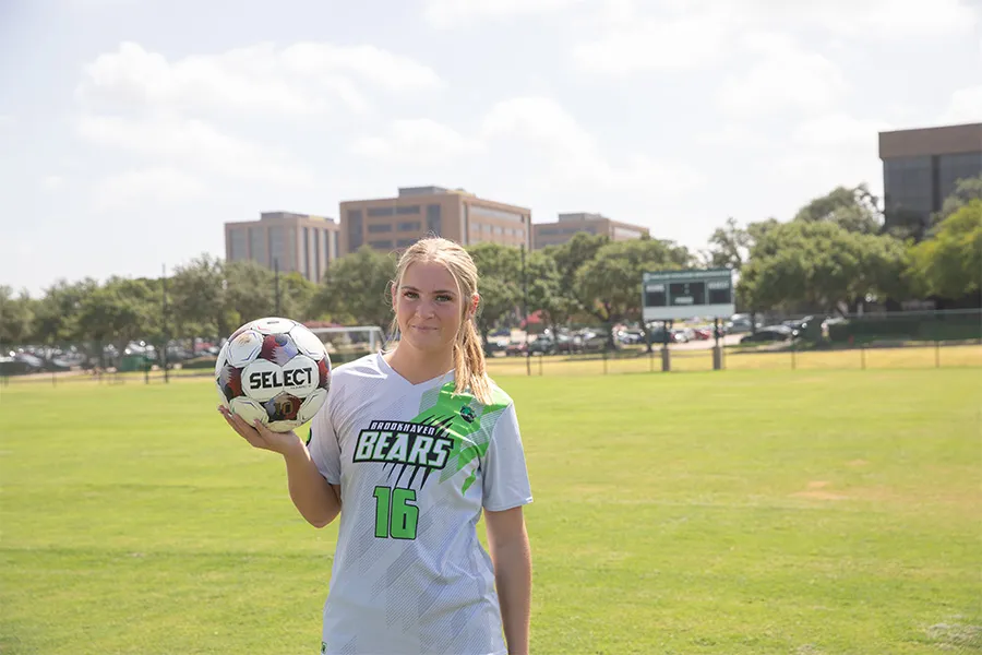 Alyssa Young stands on a field holding a soccer ball in her hand.