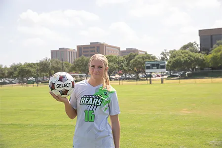 Alyssa Young stands on a field holding a soccer ball in her hand.