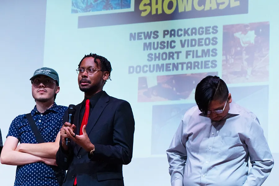 Noah Woodson on stage with two other students holding a microphone.