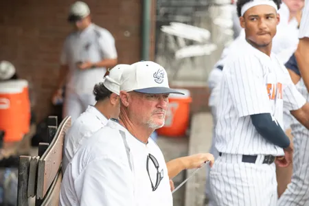 Coach in white baseball jersey and hat sitting on bench