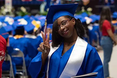 Student in commencement garb giving the peace sign.