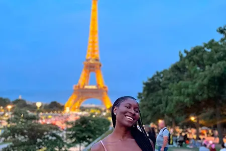Emmanuella Iwuji in front of Eiffel Tower at dusk.