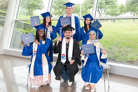 Six Dallas College students dressed in cap and gown while holding their diplomas.
