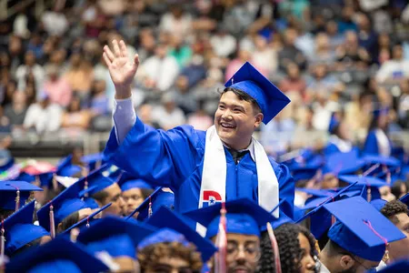 student waving in blue graduation outfit