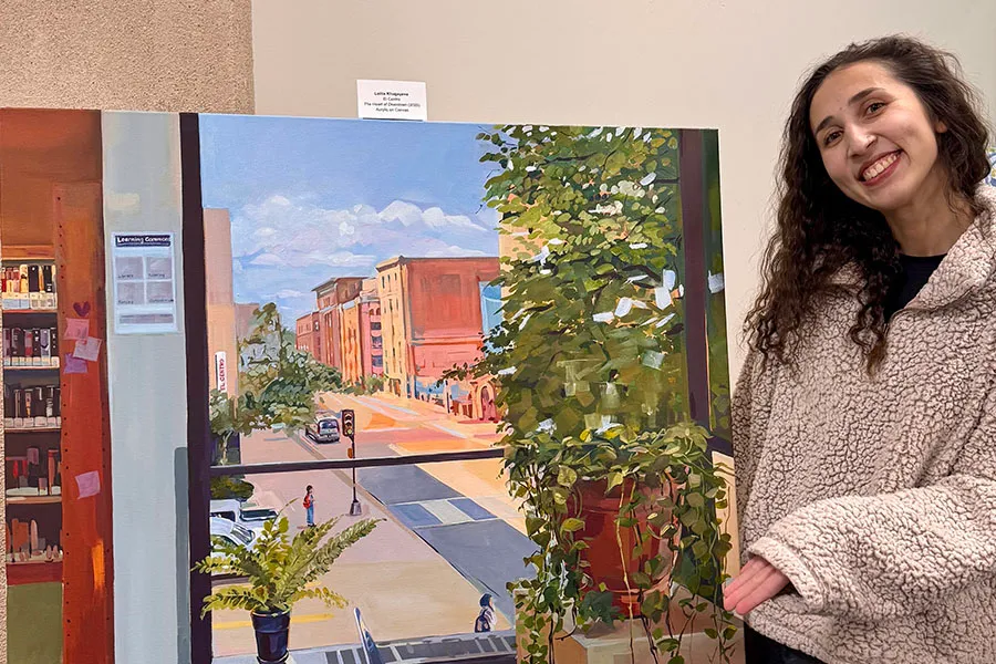 Artist Lolita Khugayeva shows off a competed painting of a downtown scene through a window.