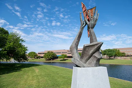 Sculpture with two hands holding a butterfly on the shore of pond.