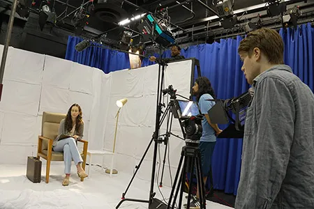 Student filming a scene with a woman sitting in a chair.