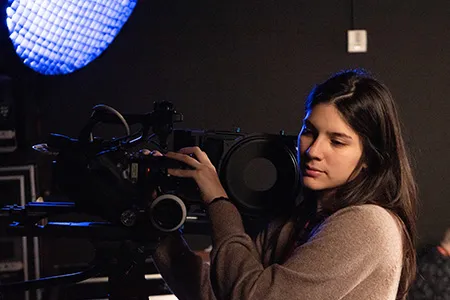 Rebekah Gonzalez stands behind a camera.