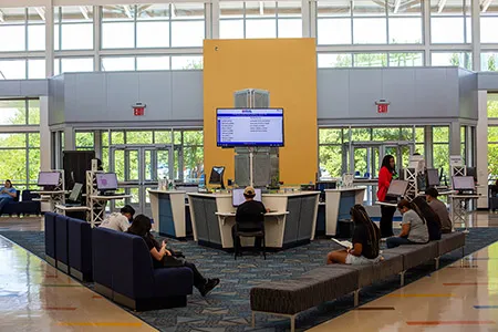 Students sitting in large waiting room with monitor overhead.