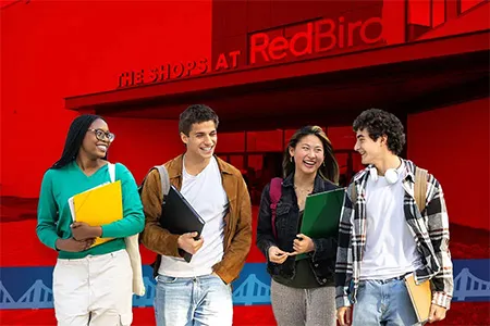 Four students stand with the Shops at RedBird behind them