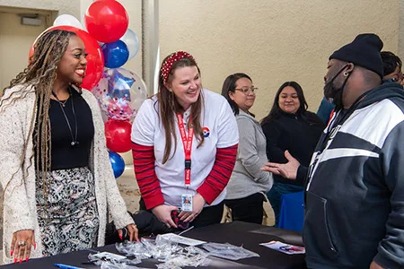 Dallas college students and employees stand around a table with balloons in the background