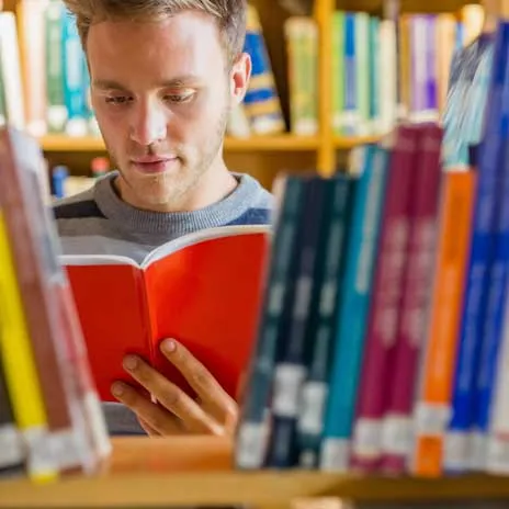 a student reading a book in between the bookshelves at a library