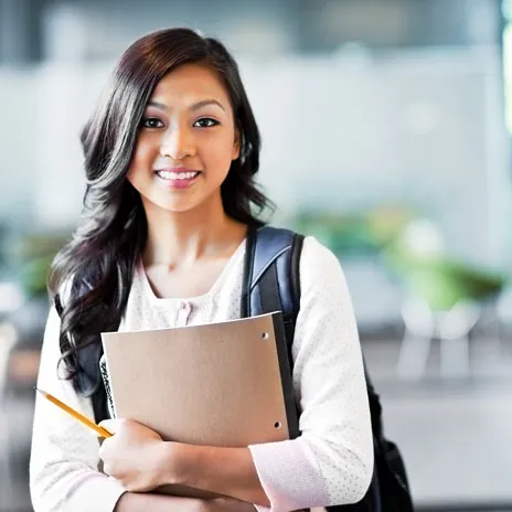 female student smiling on campus heading to class with her study materials