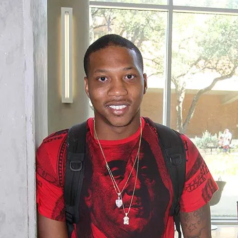 Smiling student with backpack standing indoors near window on campus