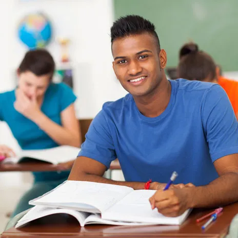 Smiling student at a desk with an open book in a classroom