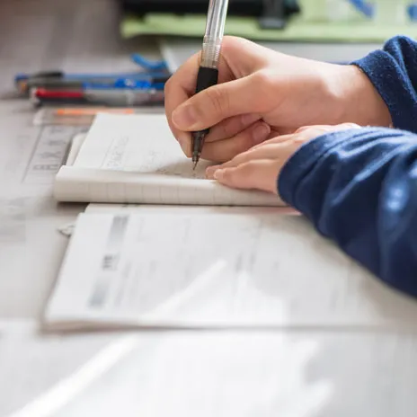 Close-up of a person filling out an application form at a desk with documents and stationery