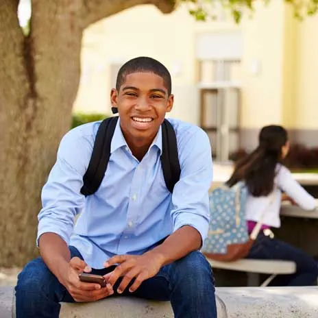 Smiling student with backpack using smartphone on college campus