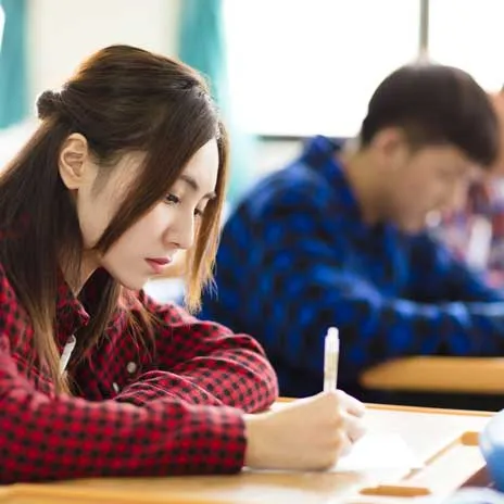 Two students in a classroom, focused on writing at their desks