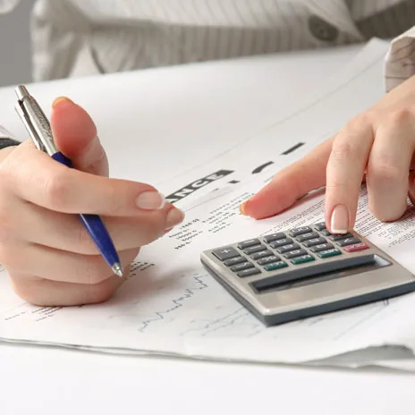 Hands using calculator and pen on financial documents.