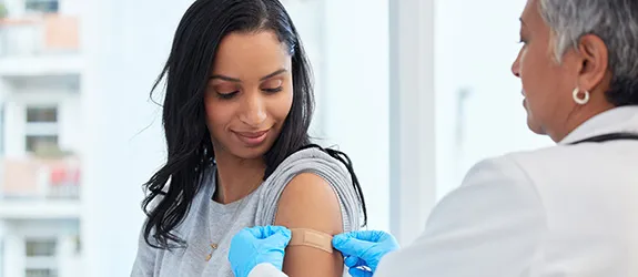 A health care worker applies a bandage to a woman's shoulder