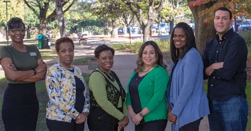 Six bilingual education staff members standing outdoors in a park-like setting.