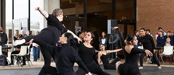 Dancers performing outdoors in front of an audience and a brick building.