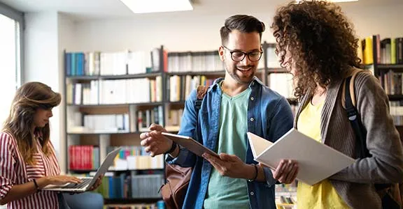 Three students with textbooks, laptops and tablets
