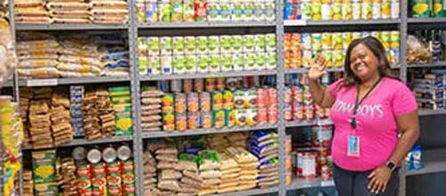 Volunteer in pink shirt at a stocked food pantry.