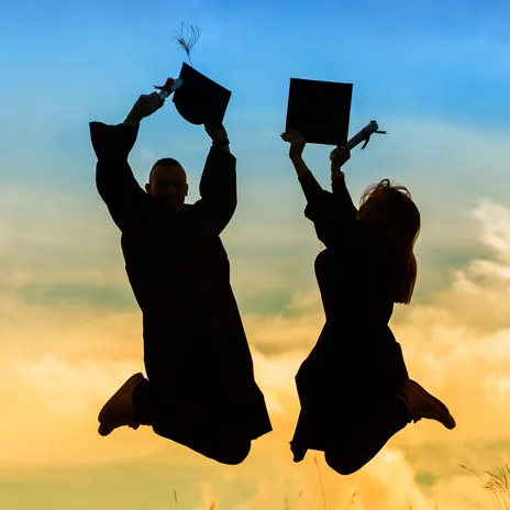 Two graduates in caps and gowns jumping joyfully against a vibrant sunset sky, celebrating their achievement