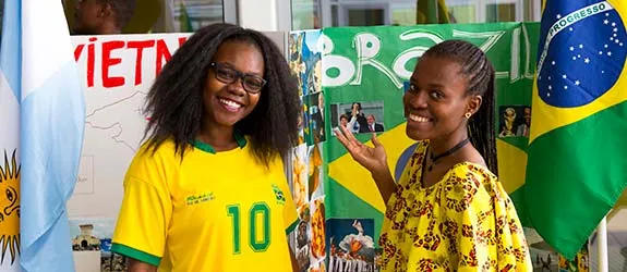 Two international students standing in front of a display with Brazil and Vietnam posters and flags.