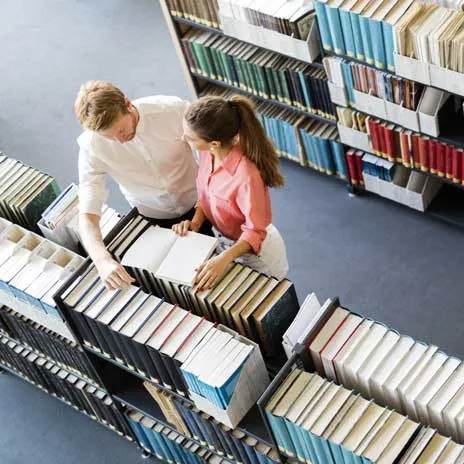 Two students reading and discussing an open book in a library