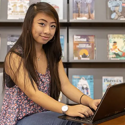 A student sits in the library and works on her laptop