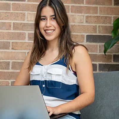 A student sits with her laptop in her lap, studying in a hallway