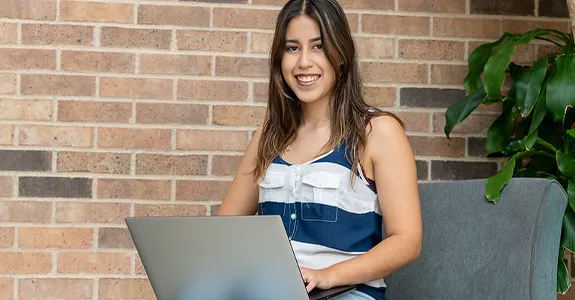 A student sits with her laptop in her lap, studying in a hallway