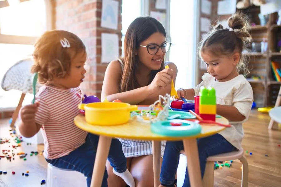 A teacher plays with two preschool students at a table