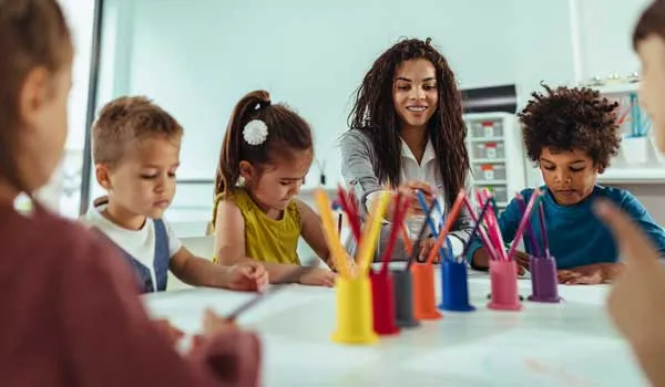 Group of kids oloring with a teacher at a table