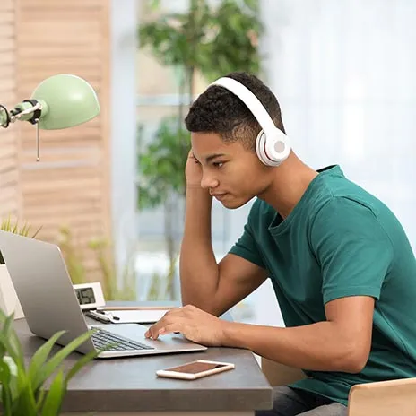 Student using a laptop at a desk with headphones on