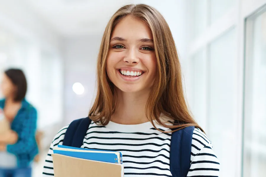 portrait of a female student smiling with notebooks in her hands