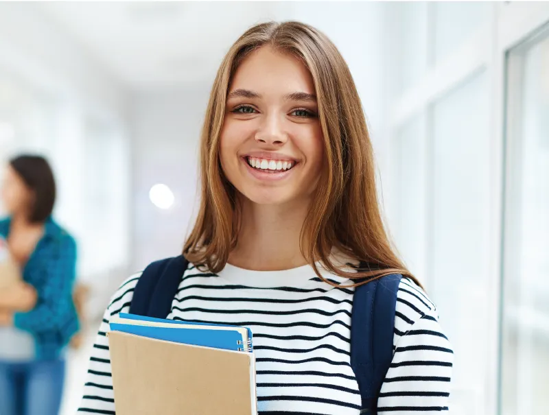portrait of a female student smiling with notebooks in her hands
