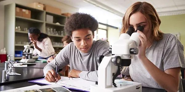 Image of two students in a classroom using a microscope