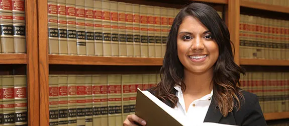 A woman dressed in a suit smiles while holding a book on law.