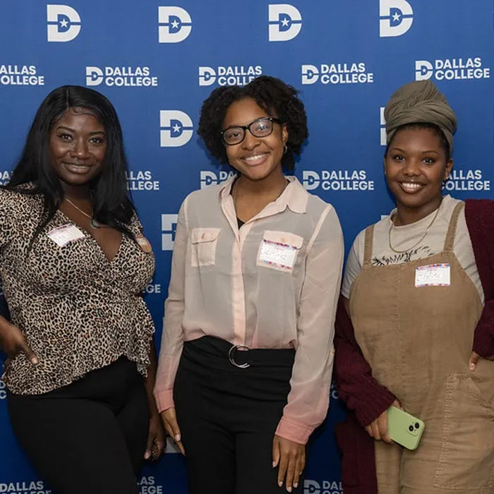 Three female students with name tags, standing before a blue Dallas College backdrop.