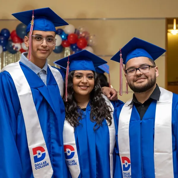 Three graduates posing with Dallas College graduation robes